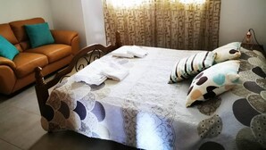 A bedroom with a bed, a wooden headboard, a brown leather sofa, and a patterned curtain. - Escape and Relax Apartment (Mandria)