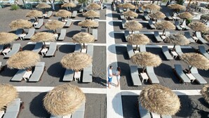 A beachside lounge area with rows of sunbeds and thatched umbrellas.