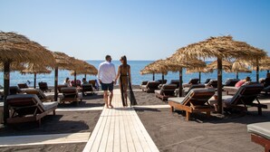 A wooden deck leading to beachside lounge chairs with thatched umbrellas, overlooking the sea.