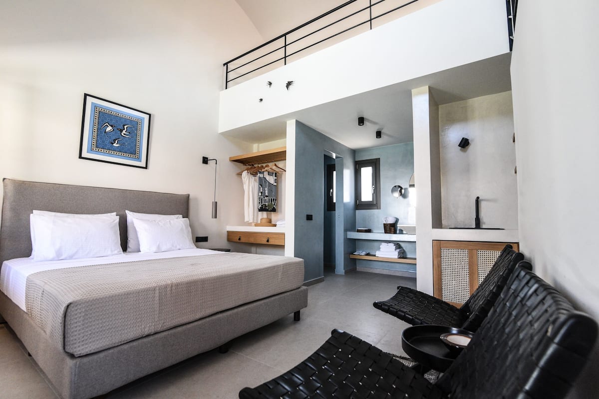 Ein Schlafzimmer mit einem Bett, einem Schreibtisch und einem Sessel. Es gibt einen Kleiderschrank und einen Spiegel.