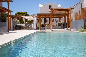 A swimming pool with a wooden pergola and outdoor seating area. - Terra Nera Suites Santorini (Santorini)