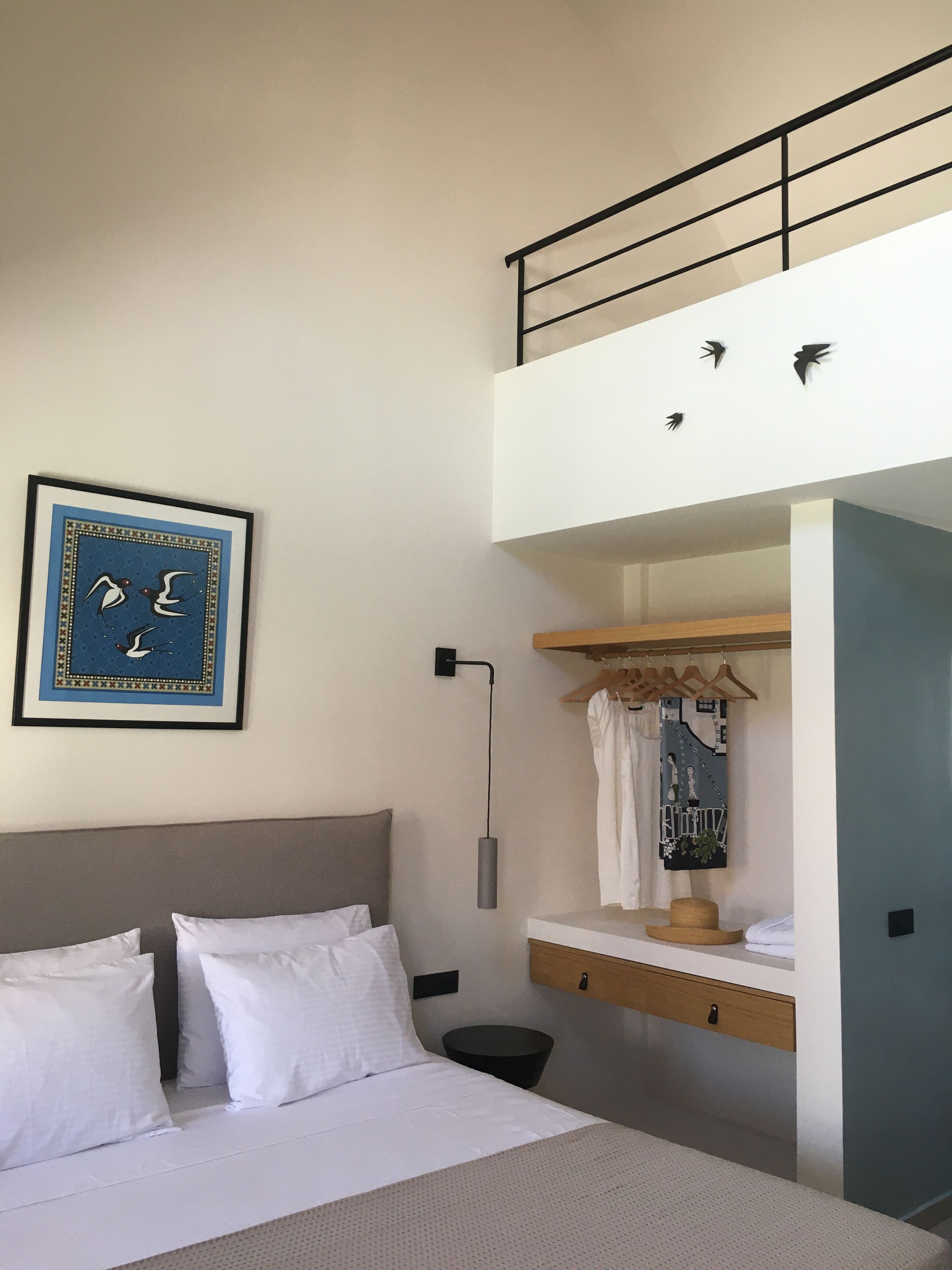 A bedroom with a bed, a nightstand, a hanging light, a wardrobe, and a ceiling with a railing.