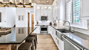 Una cocina moderna con armarios blancos, una isla central, electrodomésticos de acero inoxidable y un ventanal con persianas.