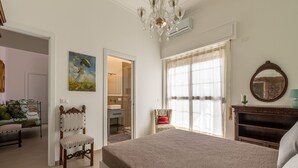 Un dormitorio con una cama grande, una silla, un cuadro, un espejo y vista al baño.