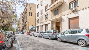 Una calle bordeada de vehículos estacionados y edificios de varios pisos con balcones.