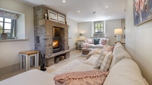 A cozy living room with a stone fireplace, a sofa set, and a dining area. - Brontë Cottage  -  3 Bedroom Riverside Cottage. Sedbergh 4 Miles. (Garsdale)