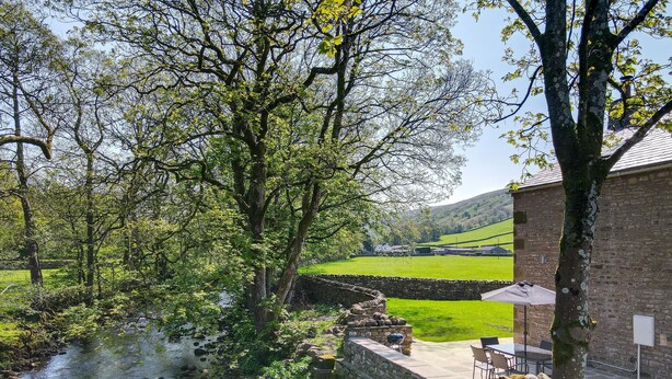 A stone wall with a seating area and a view of a river and fields. - Brontë Cottage  -  3 Bedroom Riverside Cottage. Sedbergh 4 Miles. (Garsdale)
