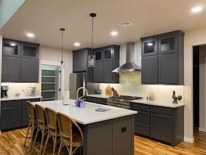 Una cocina moderna con armarios oscuros, una isla central con taburetes de bar, un refrigerador de acero inoxidable y una estufa a gas.
