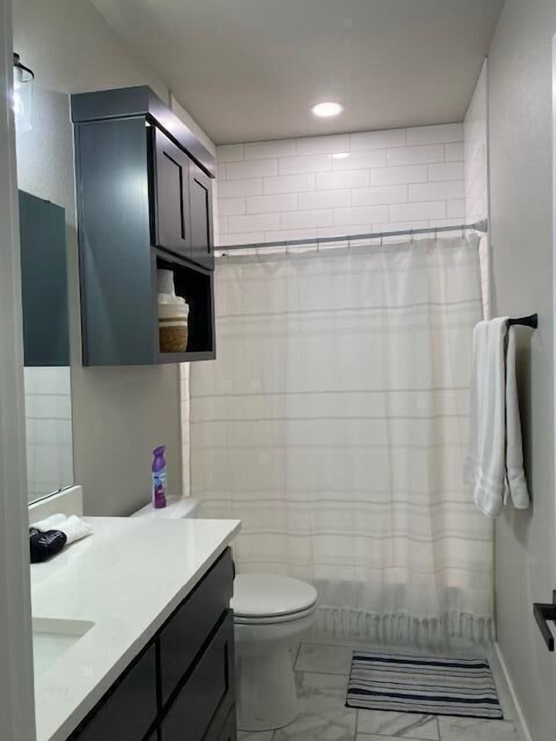 A bathroom with a toilet, a shower curtain, a sink with a mirror, and a towel rack.