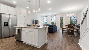 Une cuisine moderne avec des meubles blancs, un réfrigérateur en acier inoxydable et un coin repas en bois comprenant une table et des chaises.