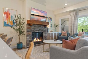 Un salon avec une cheminée en pierre, un canapé, une table basse et une vue sur l’extérieur.