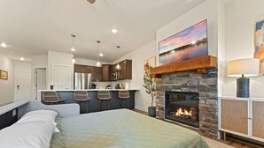 Un dormitorio moderno con una cama grande, una chimenea de piedra y una zona de cocina al fondo.