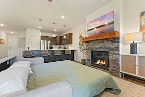 Un dormitorio moderno con una cama grande, una chimenea de piedra y una zona de cocina al fondo.