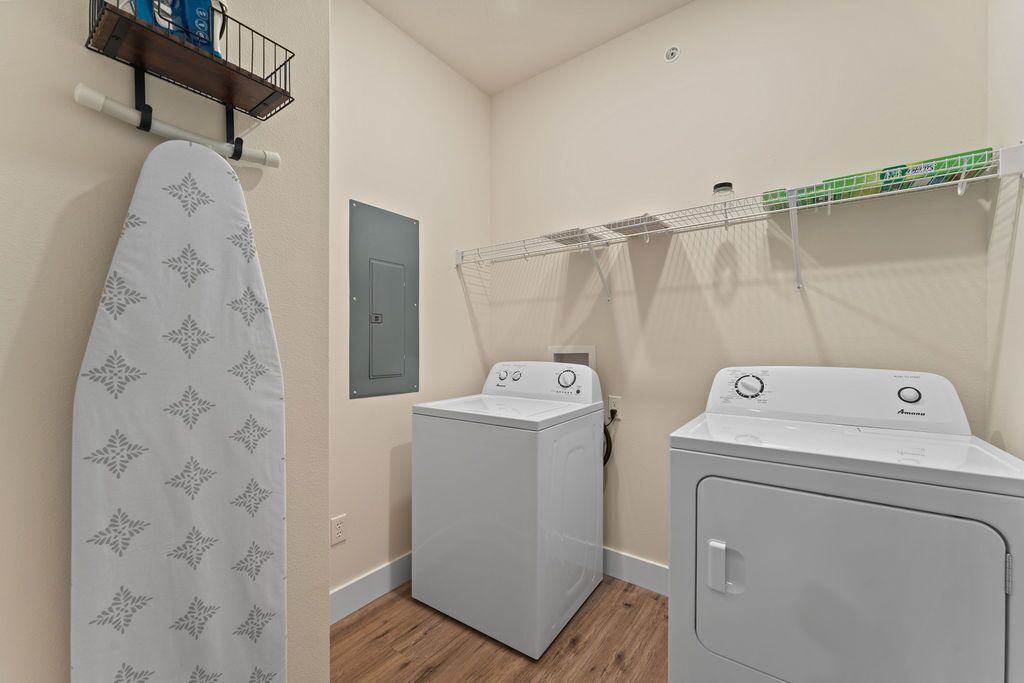 A laundry room with two washing machines, an ironing board, and a drying rack.