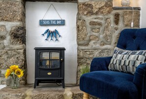 A stone wall, a black wood-burning stove, a blue sofa, and a 'Seas the Day' sign with fish decorations.