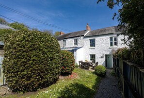 A white stone house with a garden, a wooden fence, and a gravel path.