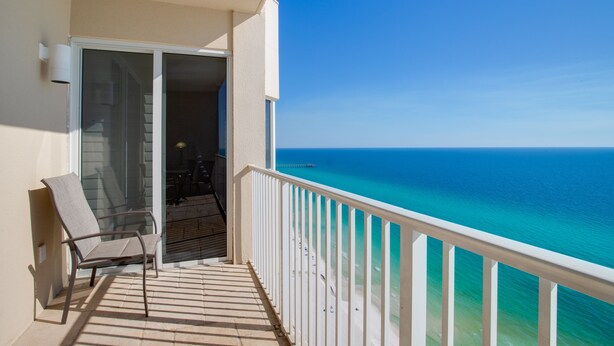 A balcony with a view of the ocean, a chair, and a door leading to an interior space.