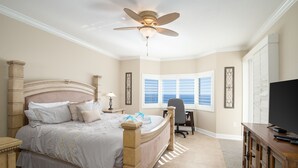 A bedroom with a large bed, a ceiling fan, a desk, and a television.