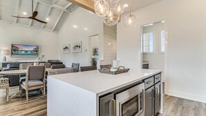 Een moderne keuken met een groot eiland, roestvrijstalen apparatuur en een eethoek met een hoge plafond en natuurlijk licht.