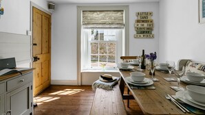 Une cuisine avec une table en bois dressée pour le repas, une fenêtre offrant une belle vue et un mur orné d’un panneau décoratif.