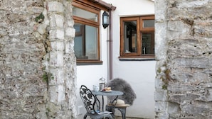 Un espace extérieur aménagé dans un style rustique, avec une table et des chaises, une lampe décorative et un mur en pierre.