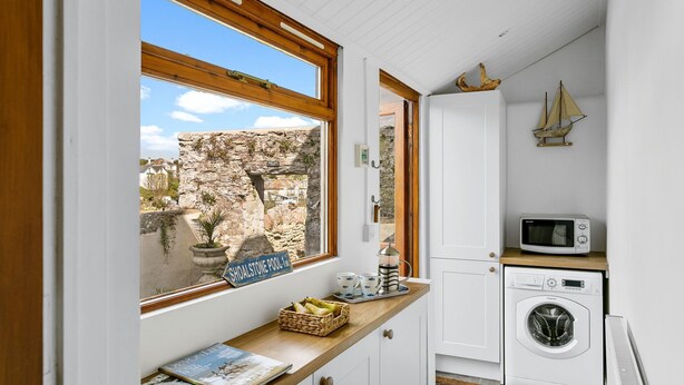 Une cuisine compacte avec un mur en pierre apparent, un lave-linge et un four à micro-ondes posés sur le plan de travail.