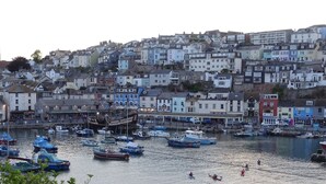 Un port où des bateaux sont amarrés, avec, en arrière-plan, une colline parsemée de bâtiments aux couleurs vives.