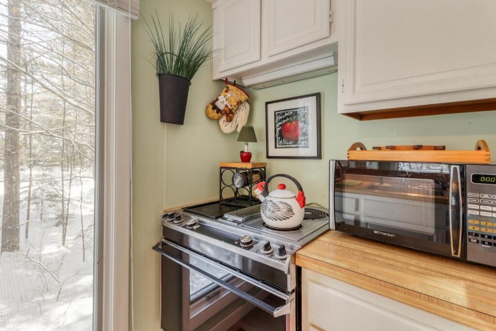 Una cocina con estufa, horno, microondas y ventana con vista a árboles.