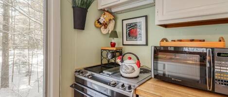 Una cocina con estufa, horno, microondas y ventana con vista a árboles.