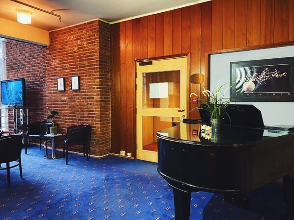 A lobby with a brick wall, a wooden door, a piano, and a framed artwork on the wall.