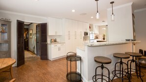 A modern kitchen with white cabinets, a central island with stools, and a dining area with a wooden table and bench.