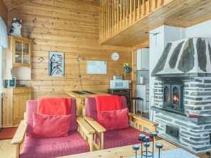 L'intérieur d'un chalet chaleureux, avec des murs en bois, une cheminée en pierre et deux fauteuils rouges recouverts de tissu.