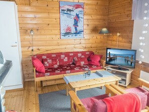 Ein gemütliches Blockhauss-Interieur mit einer Couch, einem Fernseher und einem Holzboden.