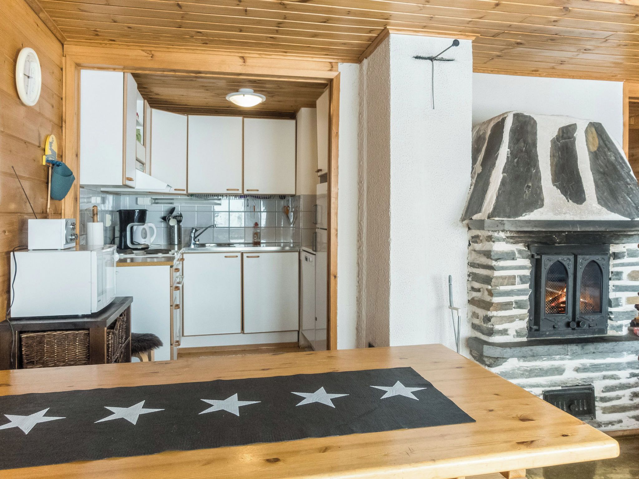 Interior de madeira com cozinha, mesa de jantar e um jogo americano com padrão de estrela, e lareira de pedra.
