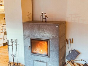A stone fireplace with a glass door, a metal stand with candles, and a log holder.