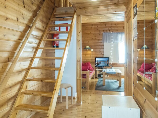 A wooden interior with a loft bedroom, a dining area, and a living room with a television.