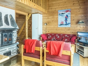 Ein gemütliches Blockhaus-Interieur mit Kamin aus Stein, Holzwänden, einer Sofagarnitur und einem Fernseher.