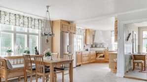 Une cuisine spacieuse avec des meubles en bois, un coin repas comprenant une table et des chaises, et de grandes fenêtres qui laissent entrer la lumière naturelle.