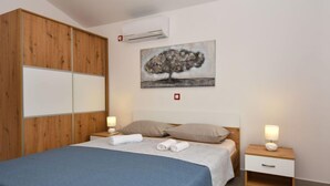 Une chambre à coucher comprenant un lit, une table de chevet, une armoire en bois et un appareil de climatisation.