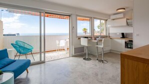 Ett modernt kök med utsikt över havet, en matplats med en blå soffa och en balkong med en stol.