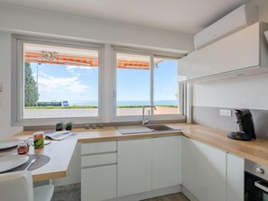 A modern kitchen with white cabinets, a wooden countertop, a sink, and a view of the sea through large windows.