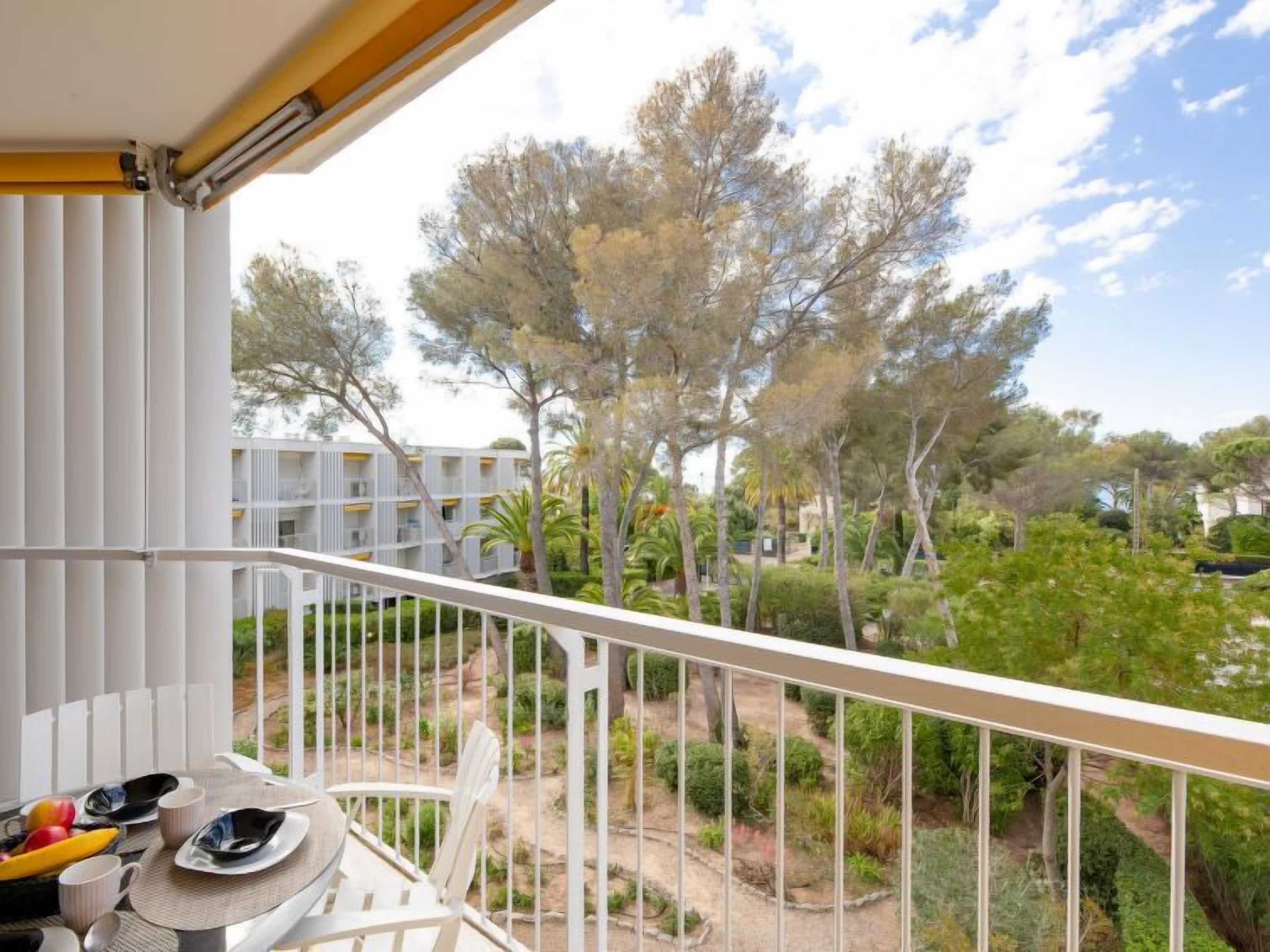 A balcony with a table set for dining, overlooking a landscaped garden and buildings.