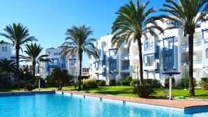A swimming pool with clear blue water, surrounded by palm trees and modern buildings with balconies. - Cala Blanca Denia by Interhome (Dénia)