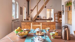 A dining area with a wooden table set for breakfast, a staircase, and a view of the kitchen.