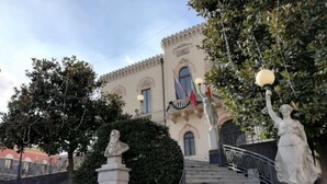 A building with a classical architectural style, featuring a central staircase with statues and a bust sculpture.