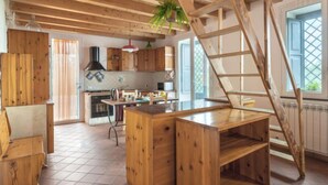 A rustic kitchen with wooden beams, a central island, and a ladder leading to a loft.