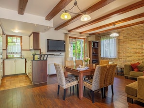 A spacious living area with a dining table, wicker chairs, a sofa, and a television.