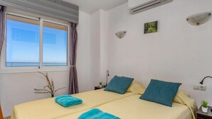 Une chambre d’hôtel avec deux lits, une fenêtre avec des rideaux, un climatiseur, une petite plante et un luminaire fixé au mur.