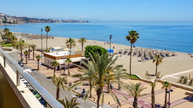 Un hôtel situé en bord de mer, offrant une vue sur l’océan, les palmiers et les parasols de plage.