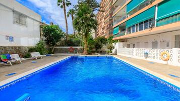 Una piscina con borde de baldosas, rodeada por una cerca blanca y palmeras.